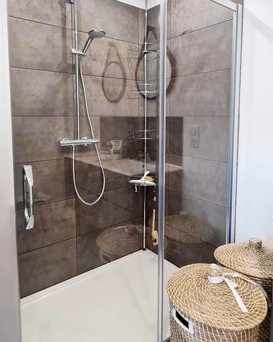 Salle de bain moderne avec baignoire encastrée en béton ciré gris, meuble vasque suspendu bleu-vert à tiroirs avec plan de toilette blanc, WC suspendu blanc, miroir cadre bois naturel