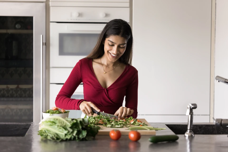 Couple dans cuisine moderne préparant repas ensemble, femme tenant verre de vin rouge, homme cuisinant à la plaque de cuisson