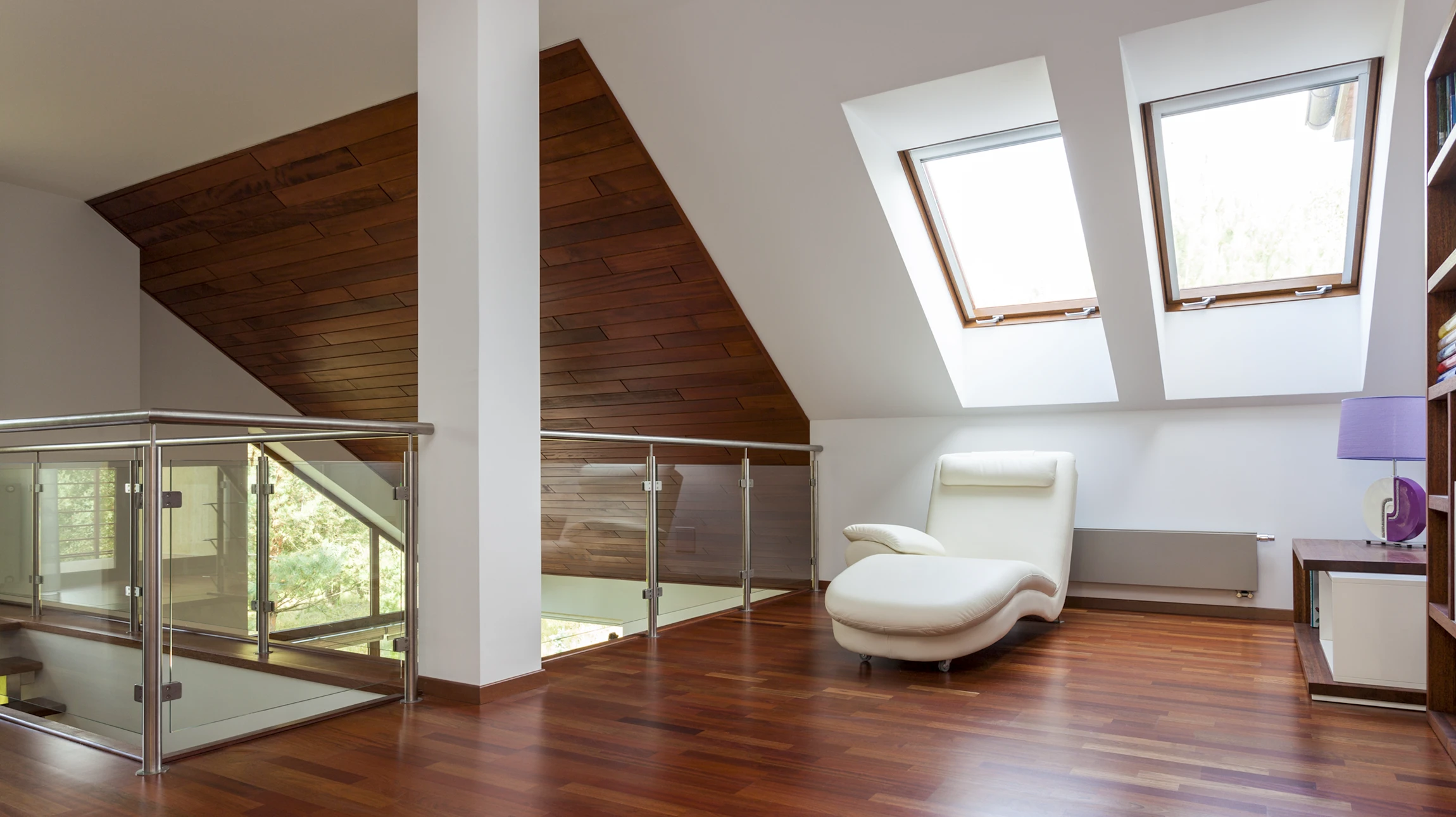 Salon moderne sous combles avec canapé d'angle violet et repose-pieds, bibliothèque noire intégrée sous pente, lampadaire design blanc
